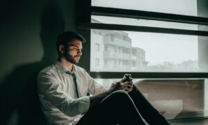 a man sitting on a window sill looking at his cell phone